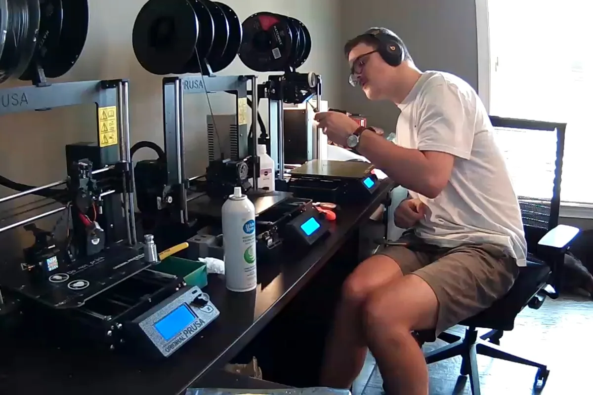 Row of Prusa 3D printers on a bench with filament spools above