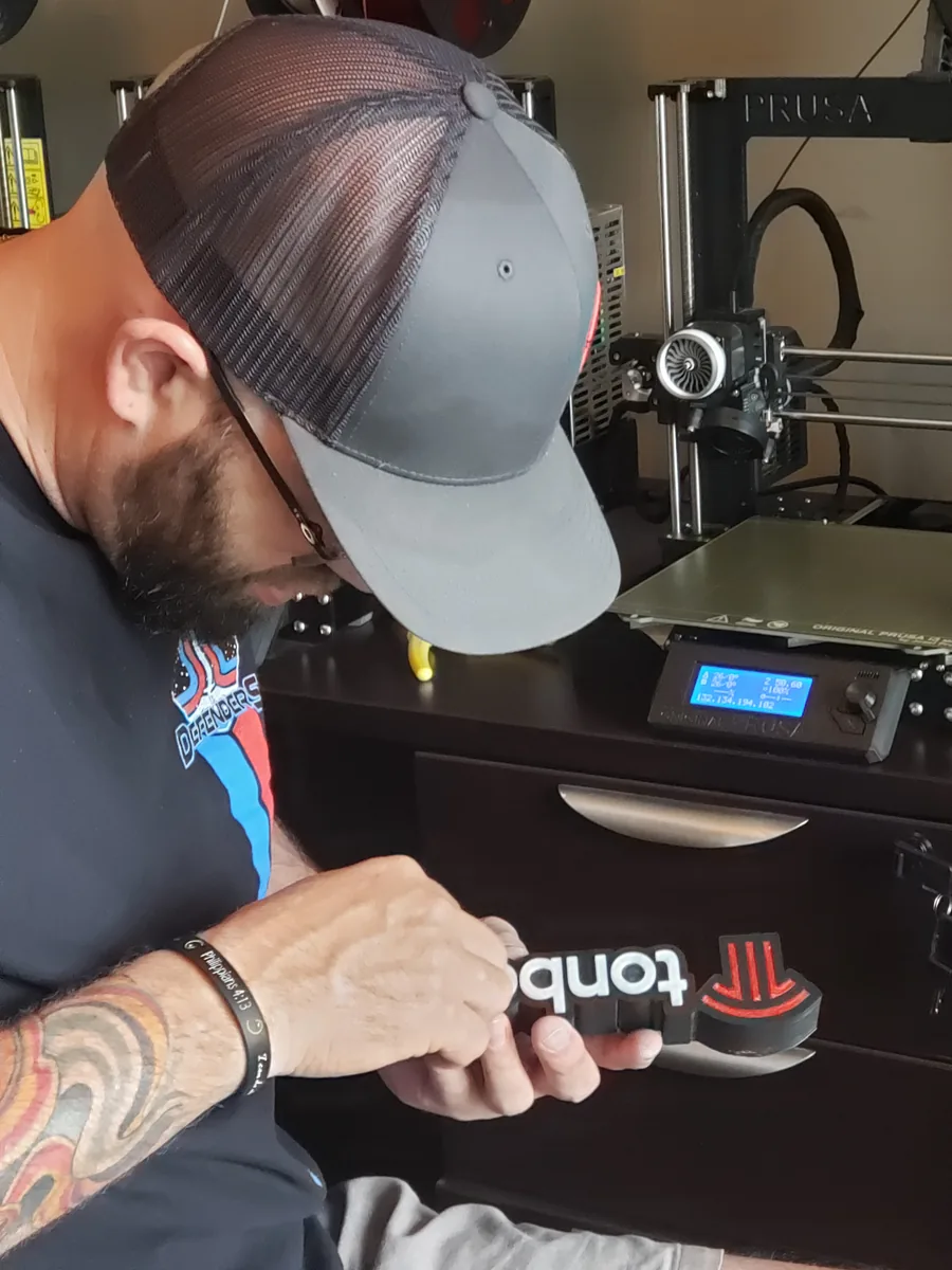 Technician checking a printed Tonbo Tech sign next to a Prusa printer